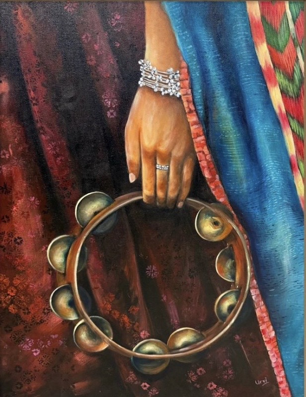 A hand holding a tambourine beside richly coloured fabric.